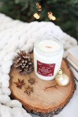 Being Wrapped In A Blanket Candle on a wooden slice with pinecone and holiday decorations.