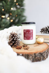 Being Wrapped In A Blanket Candle displayed on a wooden slice with pinecones, cozy ambiance for the holidays.