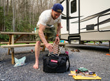 A person packing a Bugout Bag with camping gear outdoors near an RV, preparing for an adventure.