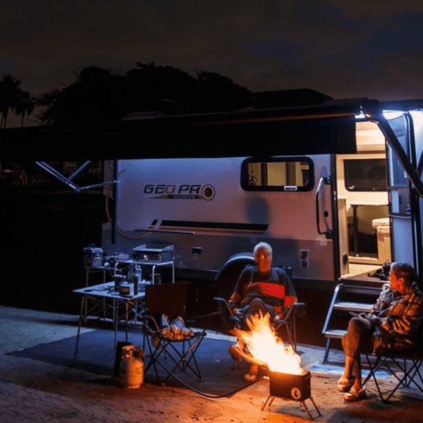 Camping at night with a GEO PRO trailer, a campfire, and two friends enjoying the outdoors.