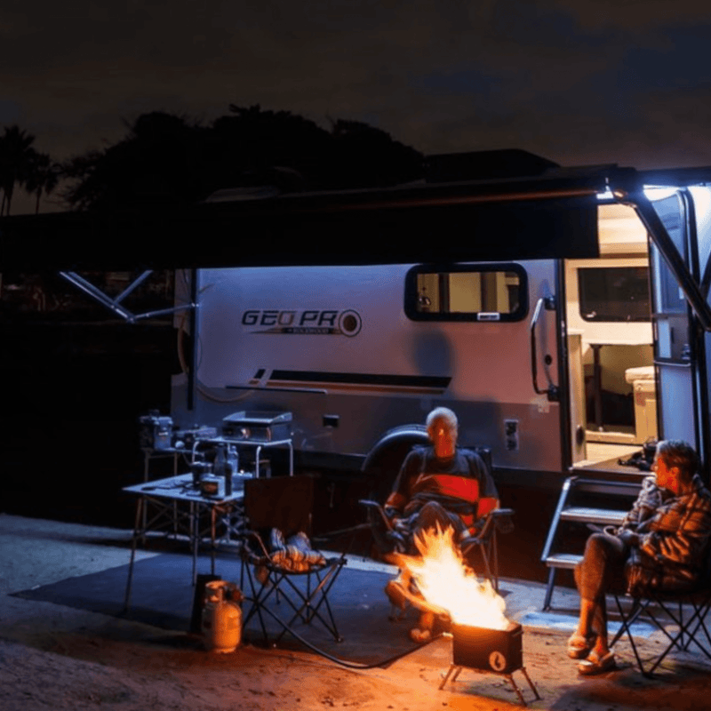 Camping at night with a GEO PRO trailer, a campfire, and two friends enjoying the outdoors.